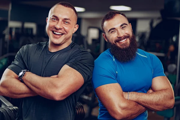 Két mosolygós, fitt férfi testépítő áll egymás mellett egy edzőteremben. — Stock Fotó