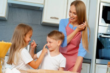 Genç sarışın kadın, anne ve çocukları hamur pişirirken eğleniyorlar.