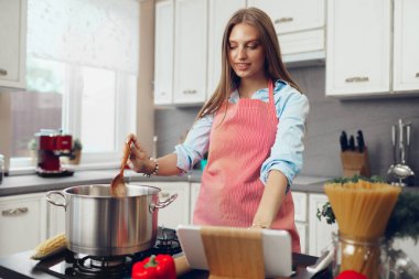 Genç ve güzel bir bayan mutfağında sobanın yanında bir şeyler pişiriyor.