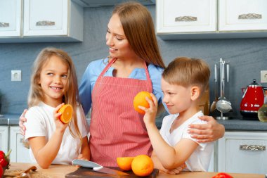 Anne çocuklarıyla mutfakta yemek pişiriyor.