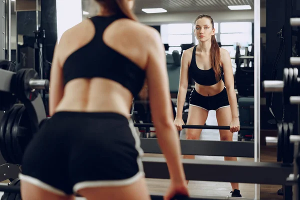 Genç bir kadın spor aletinin içinde halterle çömeliyor. — Stok fotoğraf