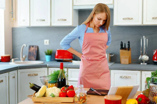 Привлекательная молодая женщина в красном фартуке стоит на кухне — стоковое фото