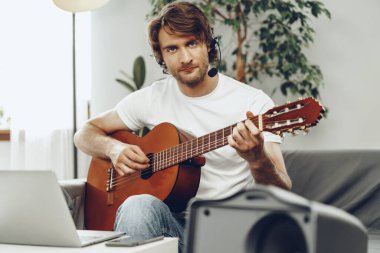 Genç adam dizüstü bilgisayarında gitar dersi izliyor.