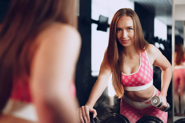 Vista posterior de una mujer entrenando sus manos con una mancuerna en un gimnasio — Foto de Stock