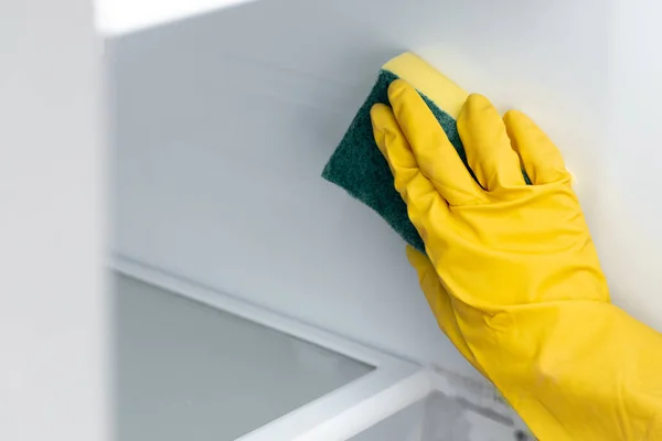 Mão de uma mulher de luva amarela limpando a prateleira do refrigerador — Fotografia de Stock