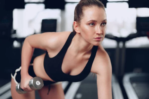 Junge brünette, sportliche Frau, die in einem Fitnessstudio mit einer Hantel trainiert — Stockfoto