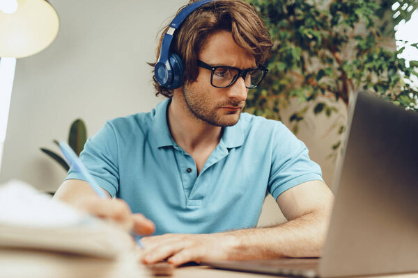 Young man in blue shirt sits at the table and studies with laptop