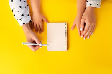 Mother and child hands writing in a notepad, top view clipart