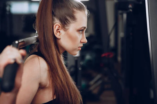 Attraente giovane donna che fa esercizi per i muscoli delle braccia e schiena in una palestra — Foto Stock