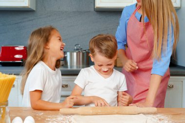 Genç sarışın kadın, anne ve çocukları hamur pişirirken eğleniyorlar.