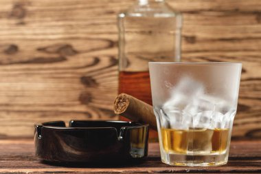 Bir bardak viski ve yuvarlanmış purolar ahşap masada.