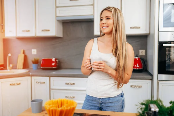 Atrakcyjna młoda kobieta pijąca herbatę stojąc w kuchni — Zdjęcie stockowe