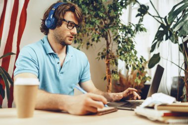 Genç sakallı iş adamı dizüstü bilgisayarı ve Amerikan bayrağıyla masada oturuyor.