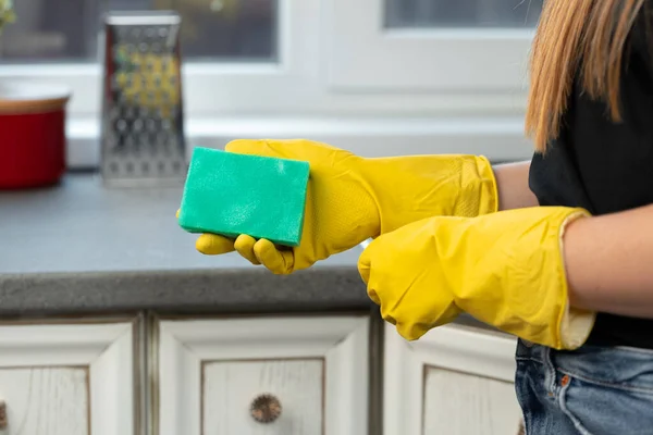 Hands of a woman in yellow gloves holding green sponge — Stock Photo, Image