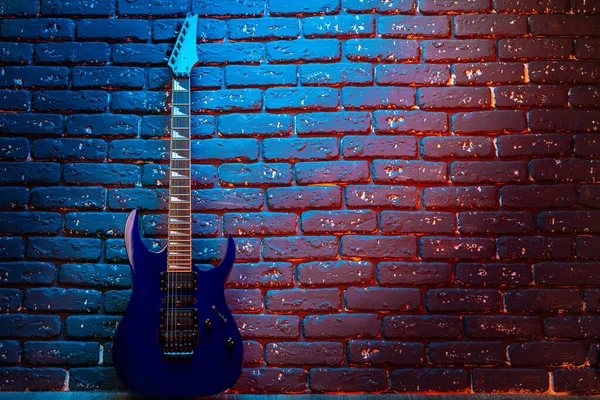 Electric guitar in neon light against dark walll