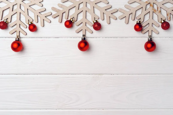 Fiocchi di neve intagliati in legno con palline rosse su sfondo di legno bianco — Foto Stock