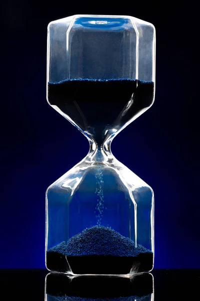 Hourglass φωτίζεται σε σκούρο μπλε φόντο από κοντά — Φωτογραφία Αρχείου