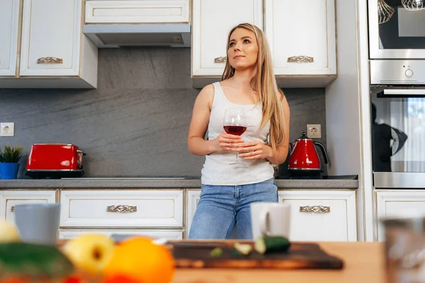 Jovem mulher atraente relaxando com vinho em sua cozinha — Fotografia de Stock