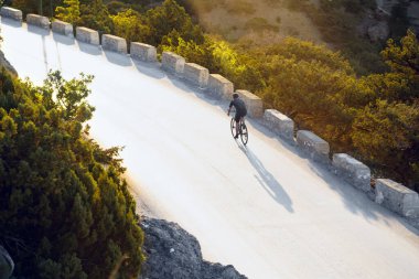 Bisikletli, sahil yolunda bisiklete biniyor.