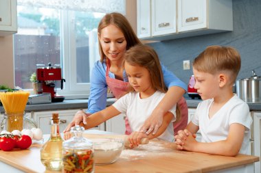 Anne ve küçük çocukları, kız ve erkek, mangırı hazırlamasına yardım ediyorlar.