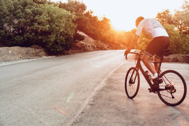 Bisikletli bir adam gün batımında açık havada bisiklet sürüyor.