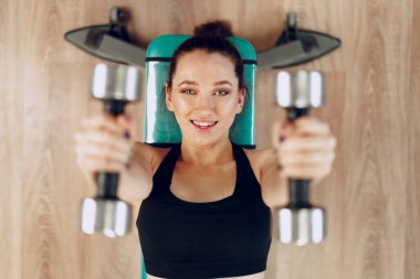 Spor salonunda halterle egzersiz yapan esmer, genç bir kadın.