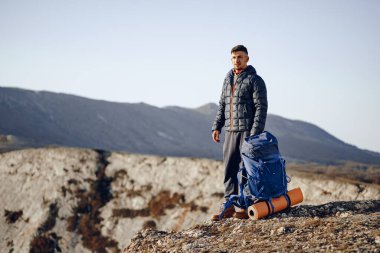 Yürüyüş ekipmanlı bir erkek sırt çantası dağın tepesinde duruyor.