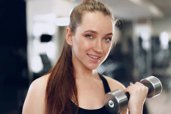 Junge brünette, sportliche Frau, die in einem Fitnessstudio mit einer Hantel trainiert — Stockfoto