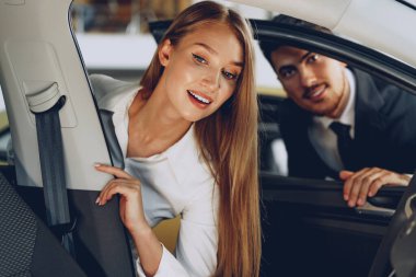 Erkek araba satıcısı bir kadına yeni bir araba gösteriyor.