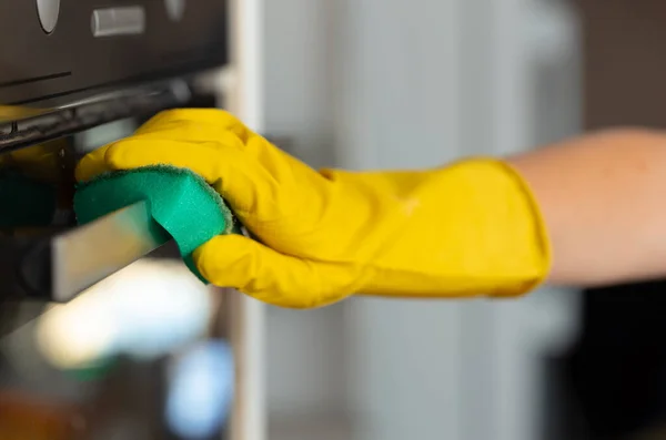 Womans hand in yellow glove cleaning door of an oven — Stock Photo, Image