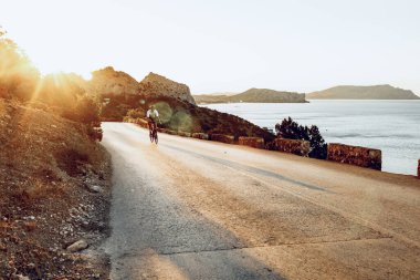 Bisikletli, sahil yolunda bisiklete biniyor.