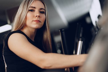 Çekici genç sarışın kadın kardiyo eğitim aparatı üzerinde egzersiz yapıyor.