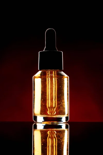 Butelka szklana z olejkiem kosmetycznym na ciemnym tle — Zdjęcie stockowe