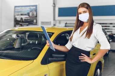 Yeni arabanın yanında koruyucu maske takan kadın araba satıcısı.