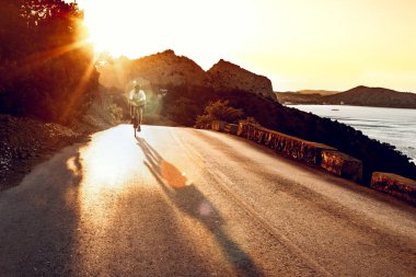 Bisikletli, sahil yolunda bisiklete biniyor.