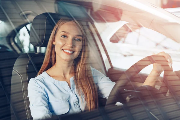 Attraktive junge Frau sitzt in Neuwagen im Showroom — Stockfoto