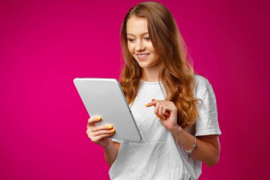 Pembe arka planda dijital tablet kullanan çekici genç bir kadın.