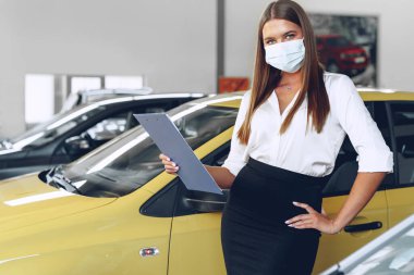 Yeni arabanın yanında koruyucu maske takan kadın araba satıcısı.