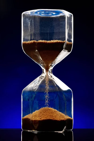 Hourglass φωτίζεται σε σκούρο μπλε φόντο από κοντά — Φωτογραφία Αρχείου