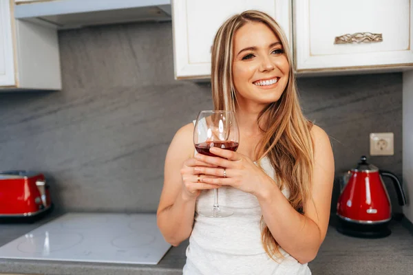 Jovem mulher atraente relaxando com vinho em sua cozinha — Fotografia de Stock