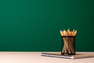 Tahta masadaki okul malzemeleri yeşil karatahtaya karşı.