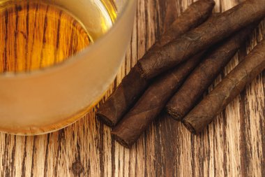 Bir bardak viski ve yuvarlanmış purolar ahşap masada.