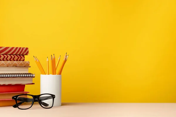 Tasse mit Bleistiften und Notizblöcken auf dem Schreibtisch vor gelbem Hintergrund — Stockfoto