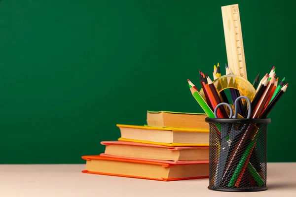 School supplies on wooden desk against green chalkboard — Stock Photo, Image