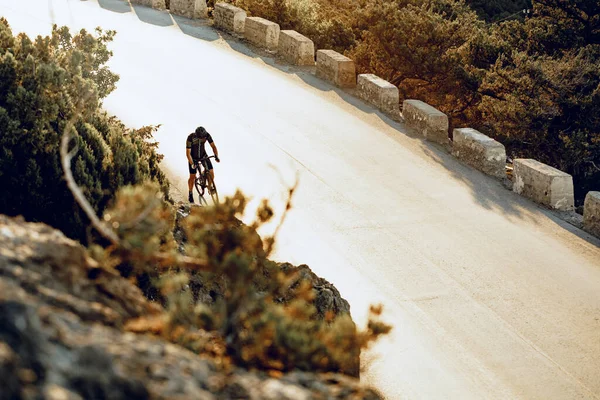 Ciclista profissional em uma estrada de montanha ao nascer do sol — Fotografia de Stock
