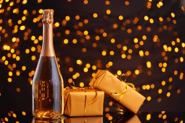 Şampanya şişesi ve Noel ışıklarının bulanık arka planına sarılmış hediye.
