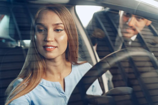 Attraktive junge Frau sitzt in Neuwagen im Showroom — Stockfoto