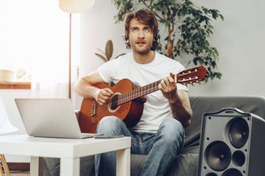 Genç adam dizüstü bilgisayarında gitar dersi izliyor.