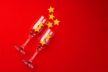 Kırmızı arka planda parıltılı konfetili şampanya bardağı düz yatıyordu.