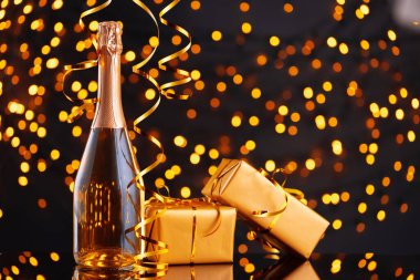 Şampanya şişesi ve Noel ışıklarının bulanık arka planına sarılmış hediye.
